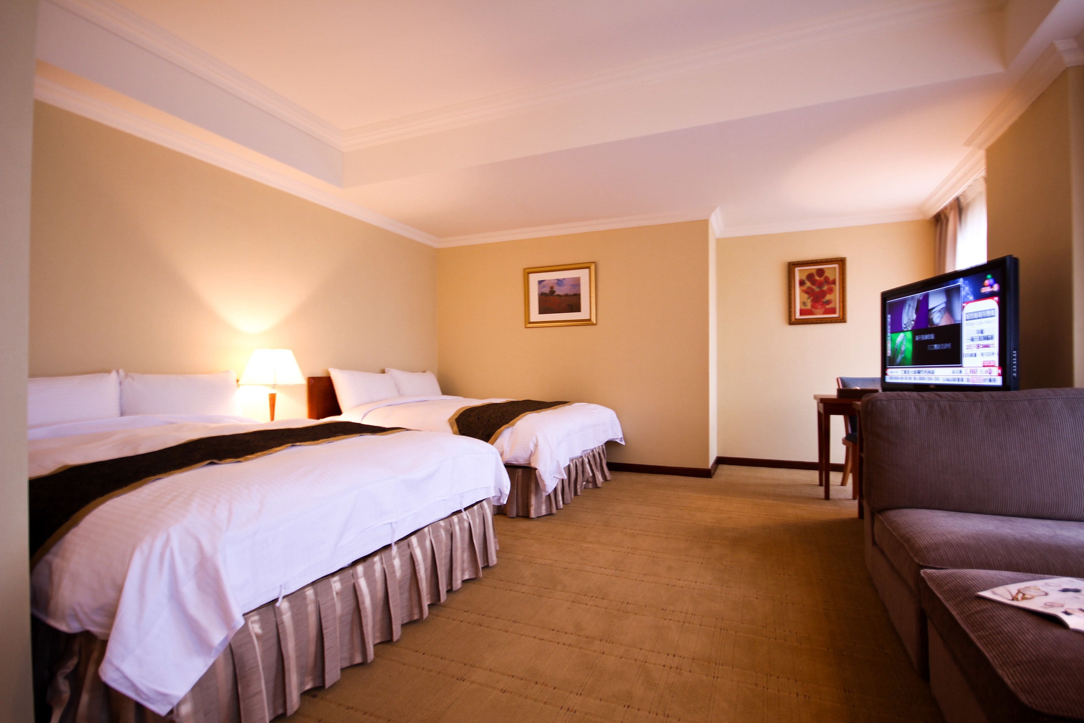 A hotel room with two beds, a sofa, a TV, and a lamp.