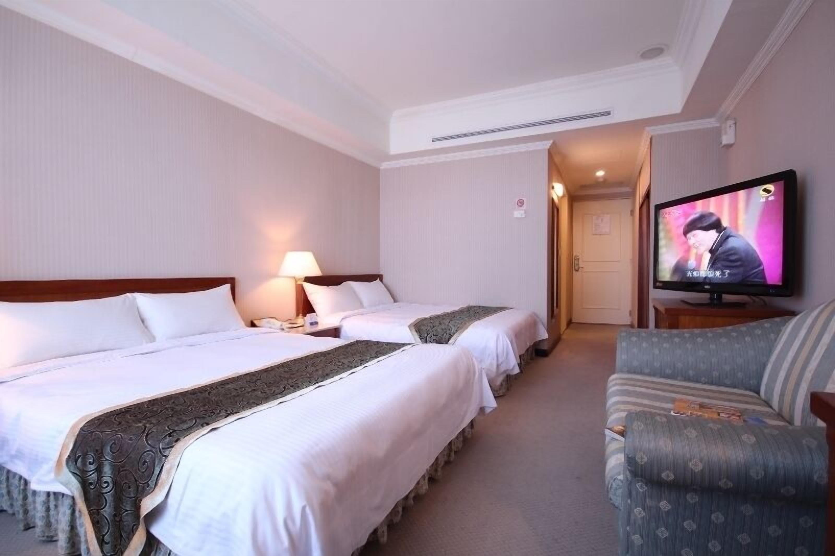 A hotel room with two beds, a television, and a sofa.