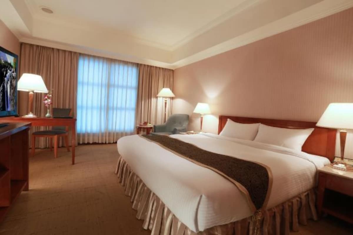 Una habitación de hotel con una cama grande, un escritorio con una silla, dos lámparas y una televisión.