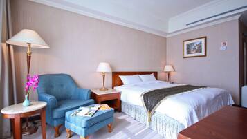 A hotel room with a bed, a chair, a small table with a lamp, and a bedside table with a lamp.