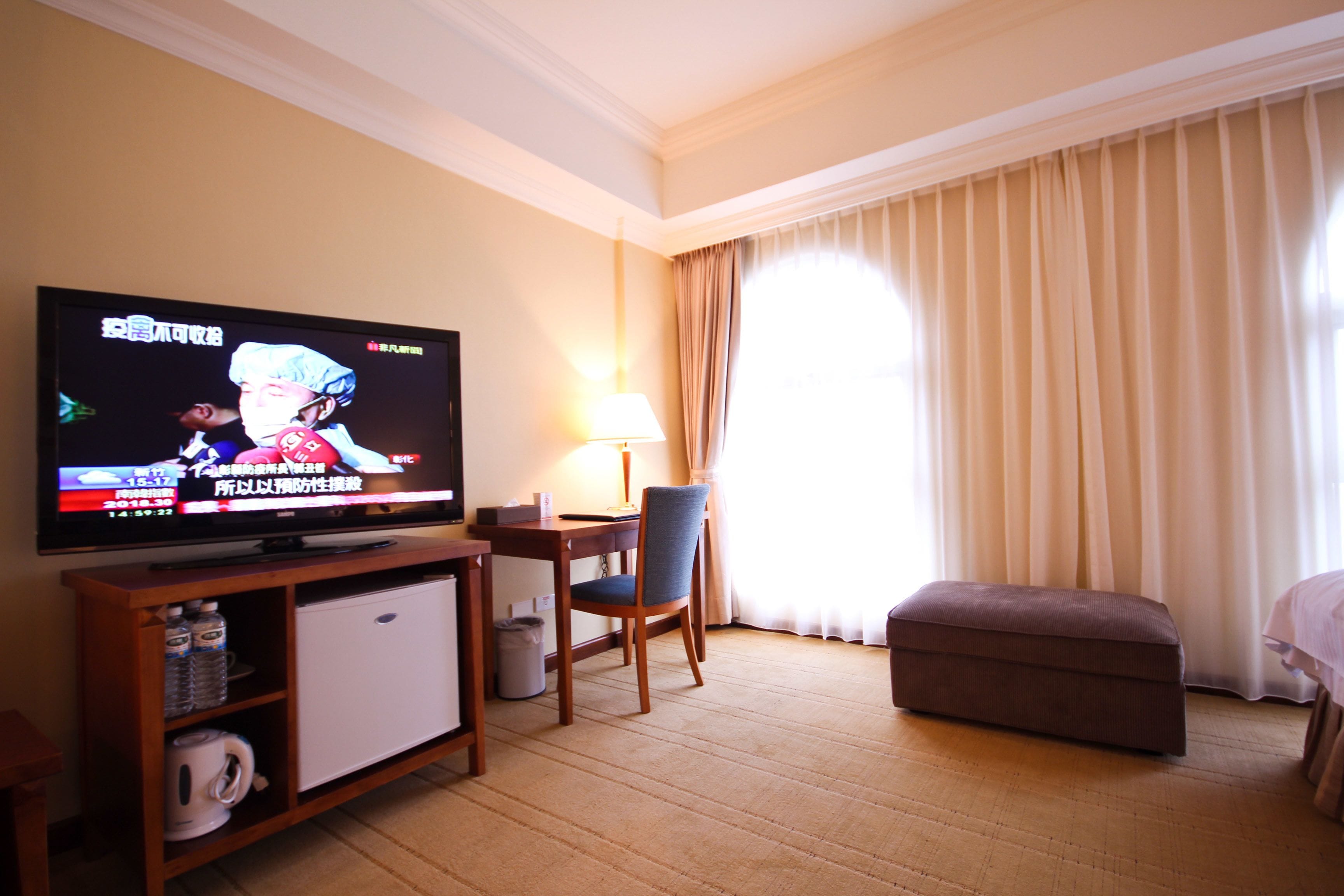 A hotel room with a television, a desk, a chair, a small sofa, and a window with curtains.