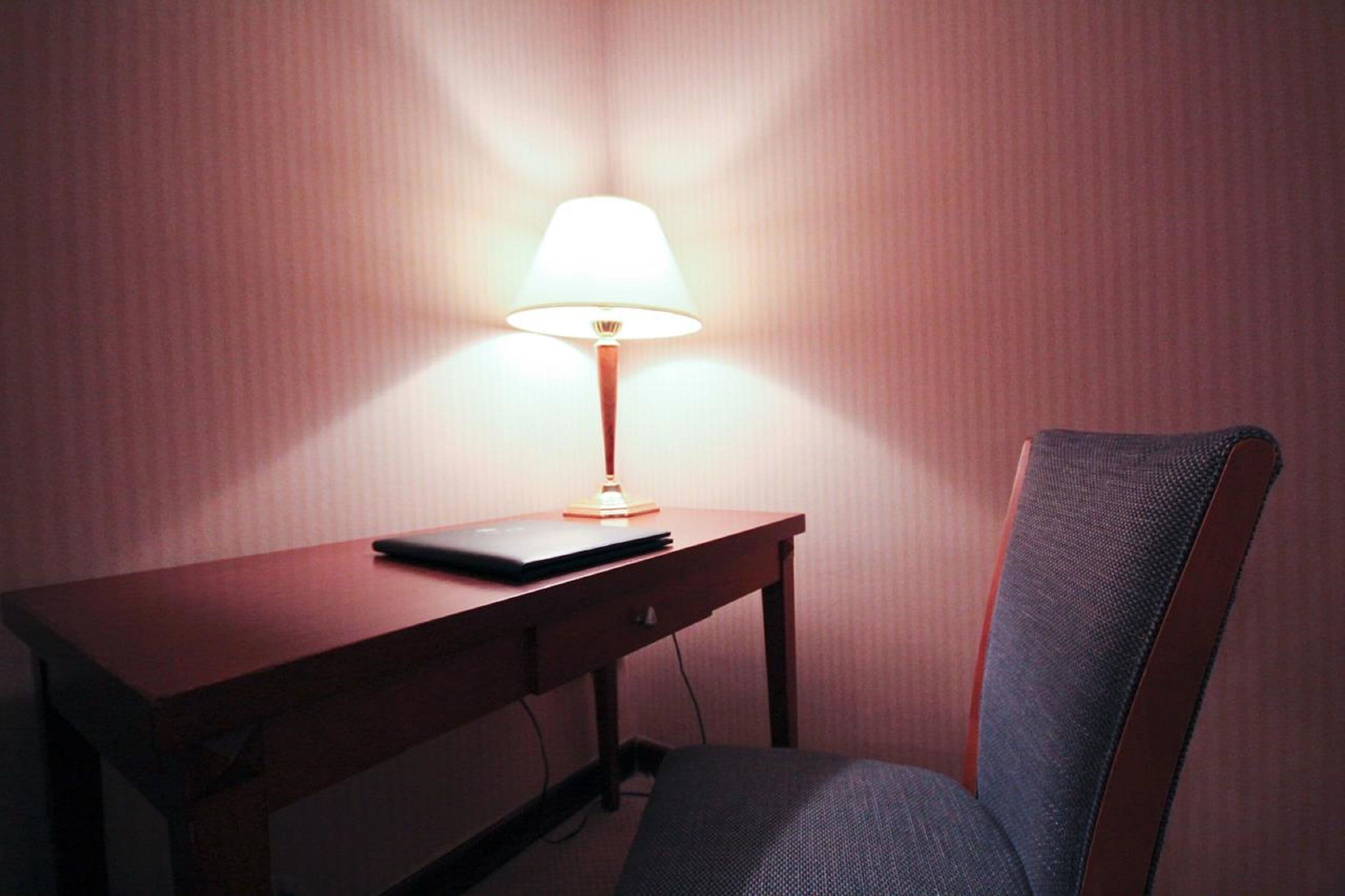 A desk with a lamp, a laptop, and a chair in a room with a plain wall.