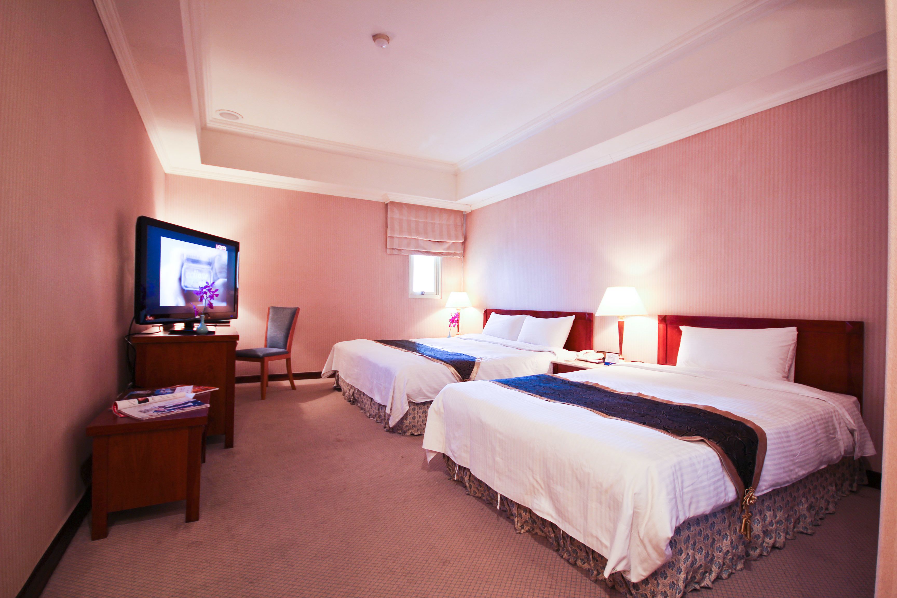 Ein Hotelzimmer mit zwei Betten, einem Fernseher auf einem Schreibtisch und einem Sessel.