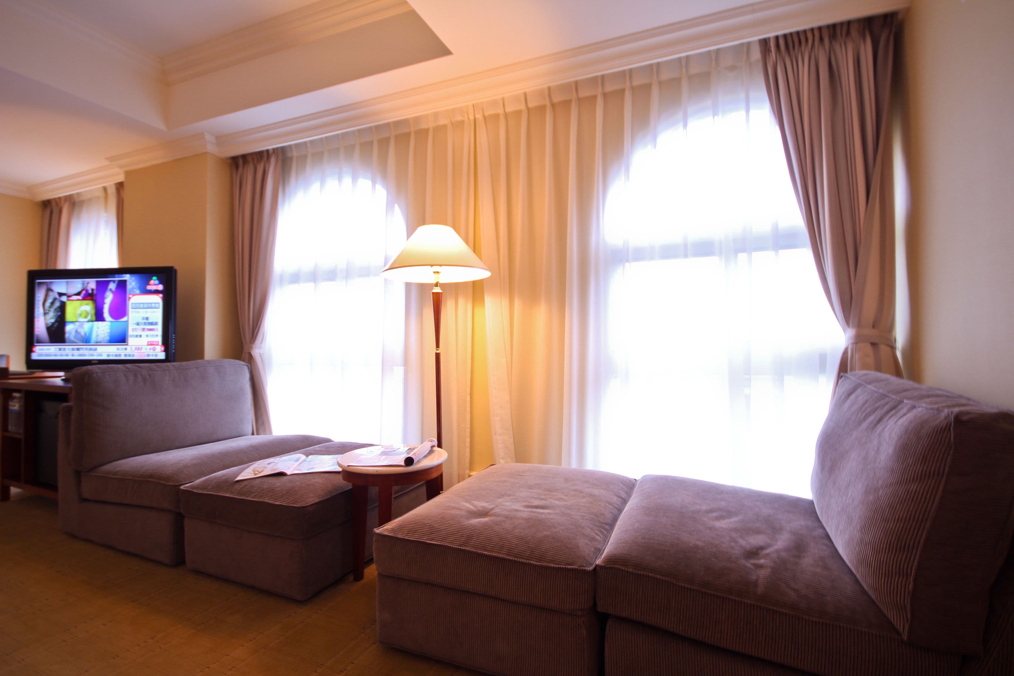 A living room with a sofa, ottoman, lamp, and a television.