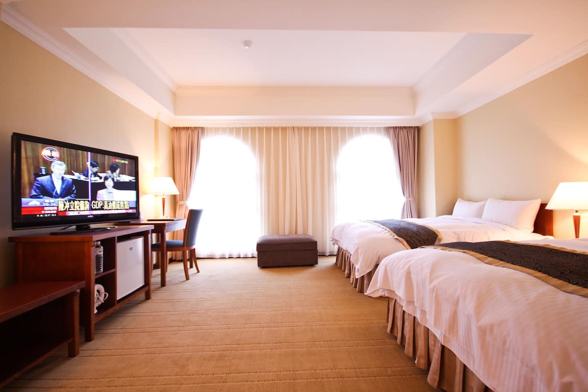 A hotel room with a television, two beds, a desk, and a chair.
