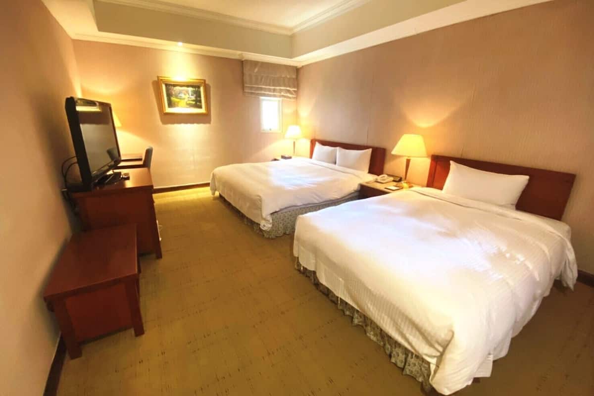 A hotel room with two beds, a desk, a television, and a framed picture on the wall.