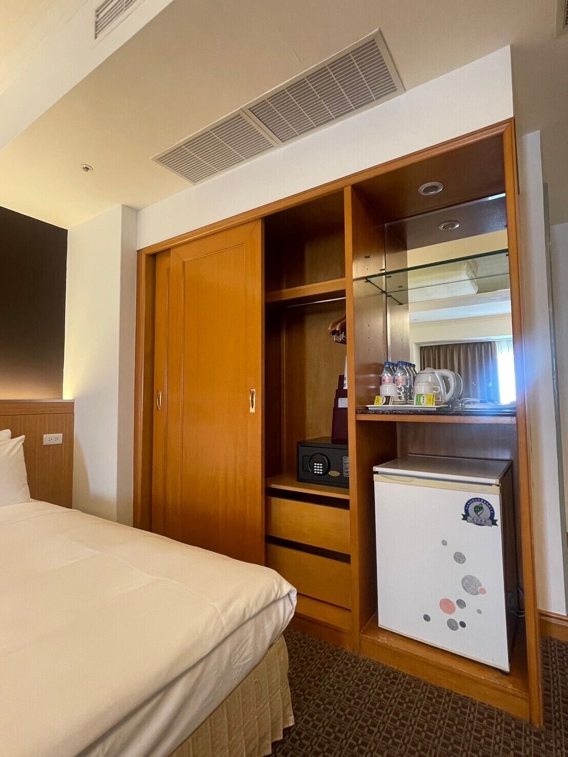 A hotel room with a bed, a wardrobe, a minibar, and a small refrigerator.