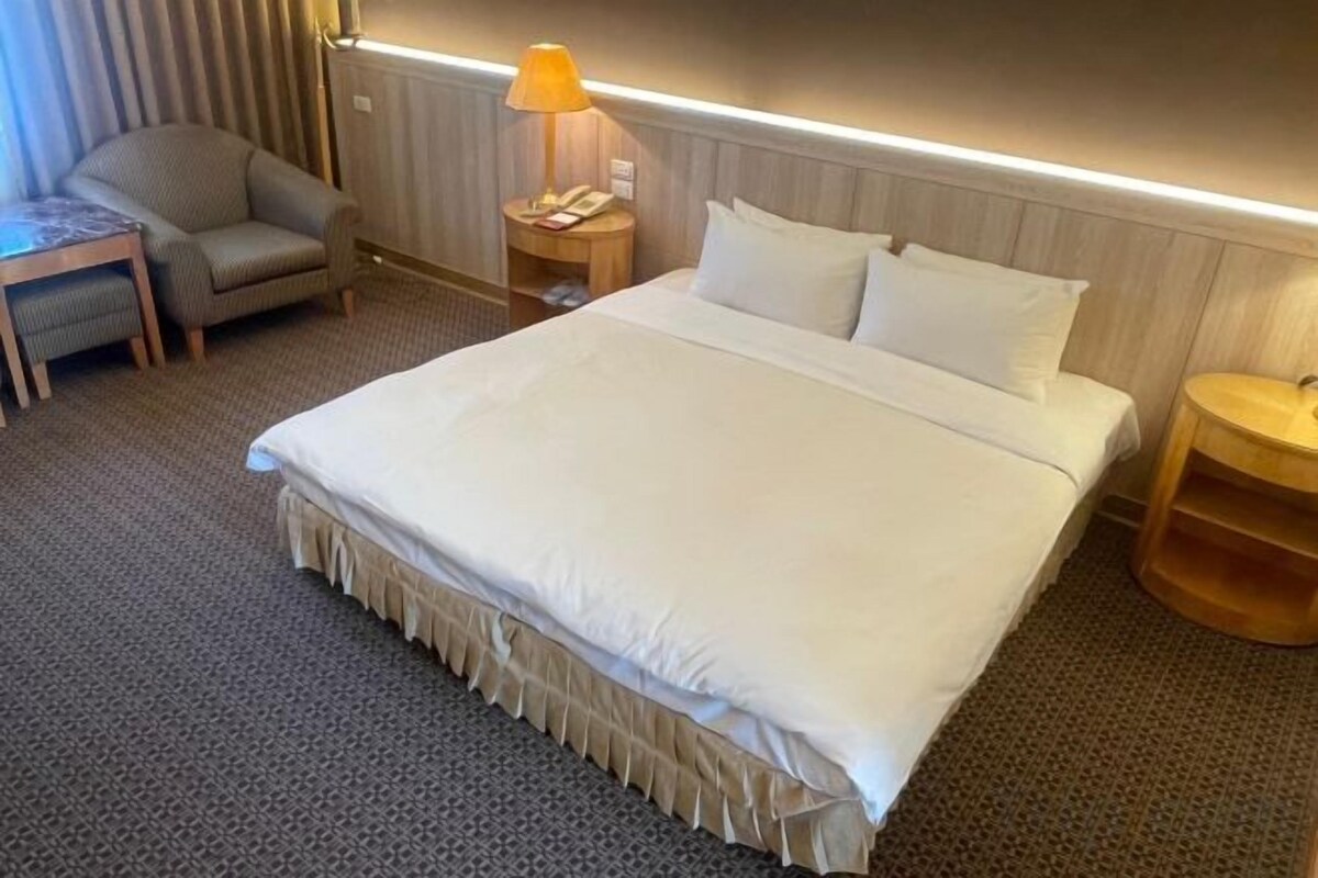 Ein Hotelzimmer mit einem großen Bett, einem Schreibtisch, einem Stuhl, einer Lampe und einem Nachttisch.