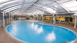 An indoor swimming pool with a curved design, surrounded by lounge chairs and a covered area with a glass ceiling. - Chuto Plaza Hotel (Taoyuan City)