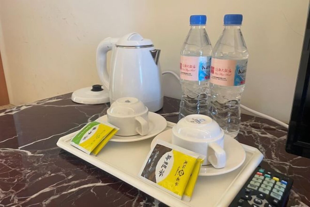 A tray with a white teapot, two bottles of water, a cup, a saucer, and two packets of tea on a marble surface.