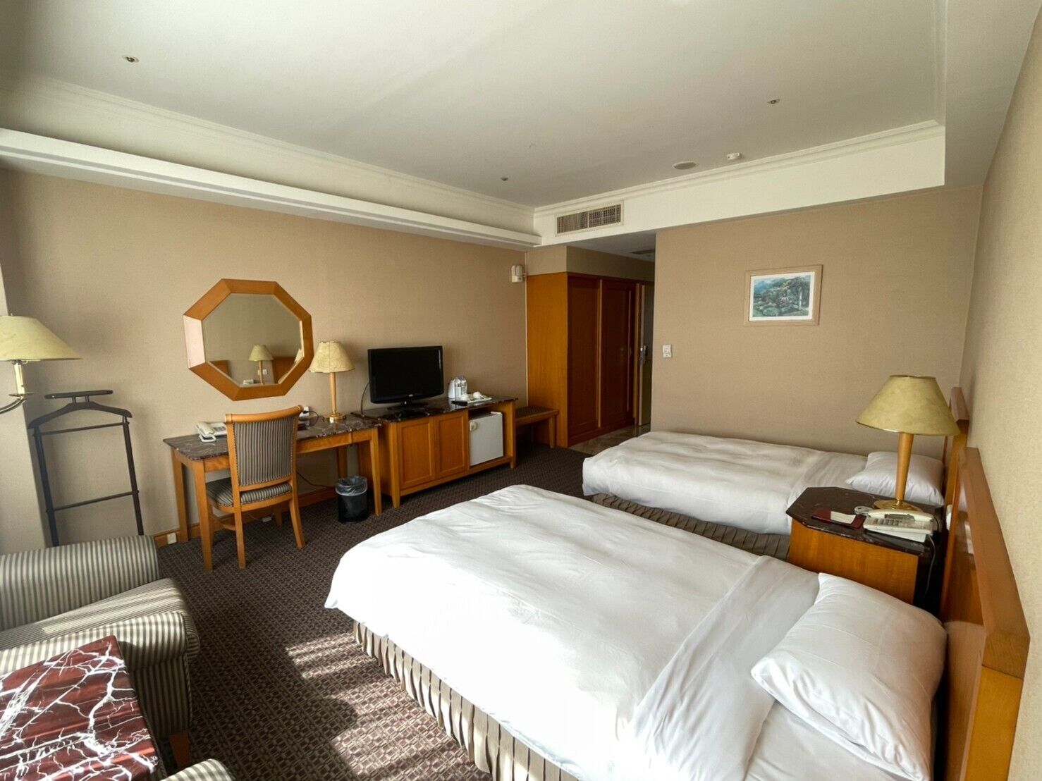 Een hotelkamer met twee bedden, een bureau met een computer, een spiegel en een televisie.