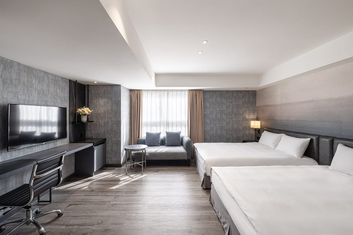 A modern hotel room with a flat-screen TV, a desk, a sofa, two beds, and a large window with curtains.