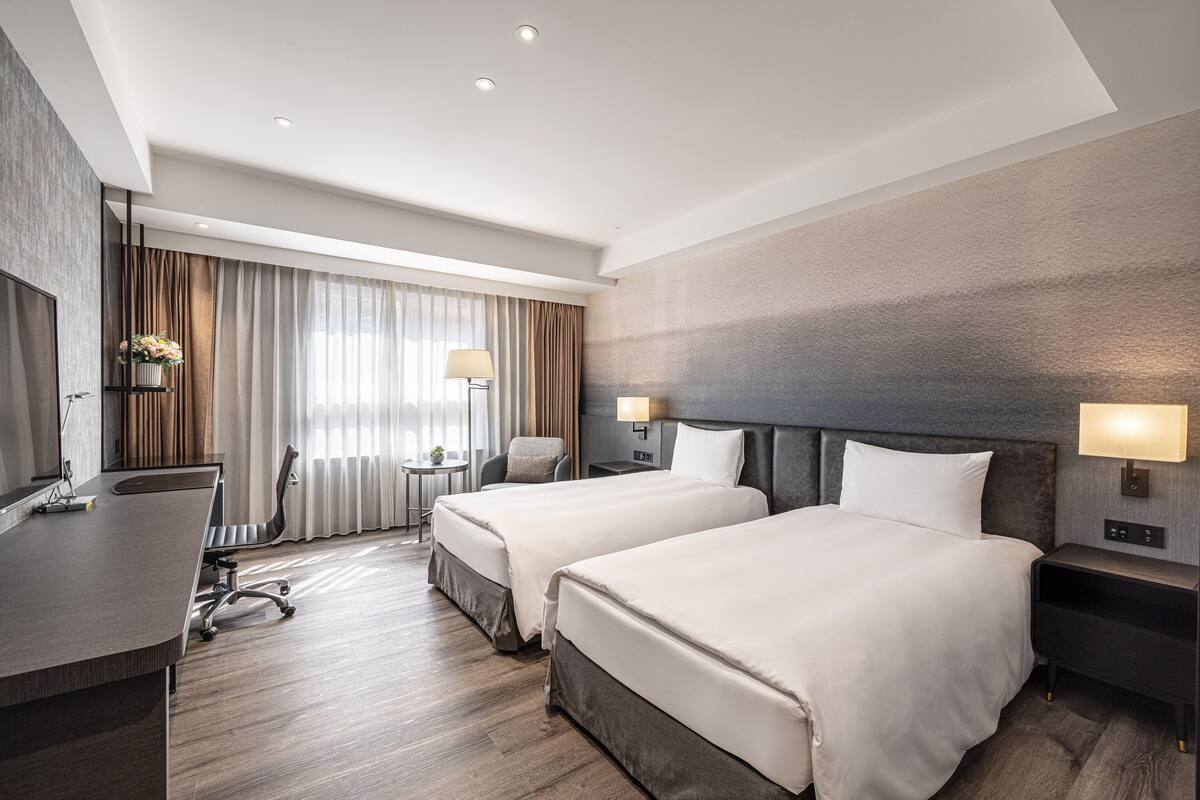 A modern hotel room with two beds, a desk, and a TV.