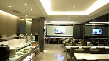 A modern dining area with a buffet, multiple tables, and chairs, and a television screen mounted on the wall.