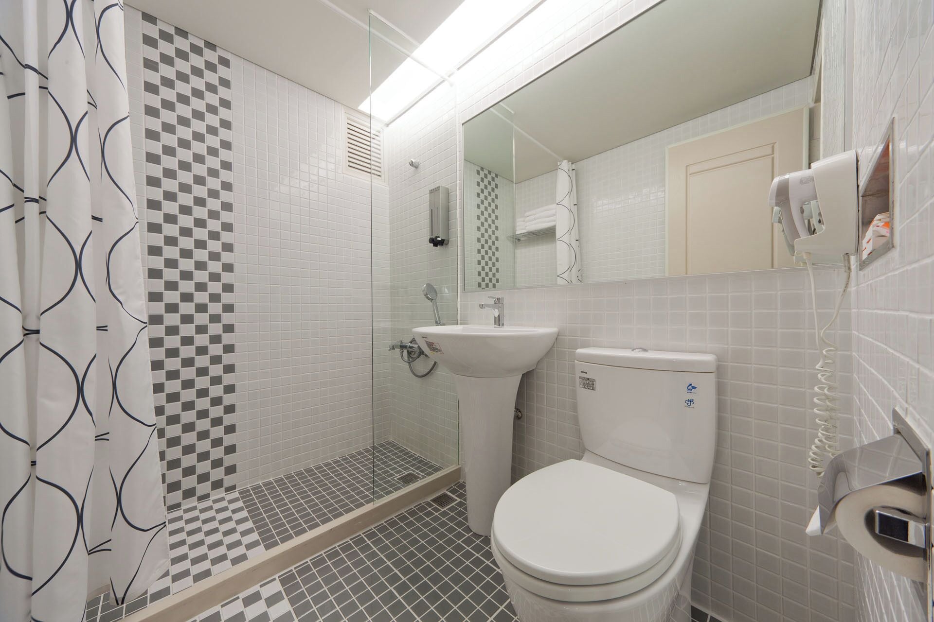 Un baño con pared de ducha a cuadros, un lavabo y un inodoro.