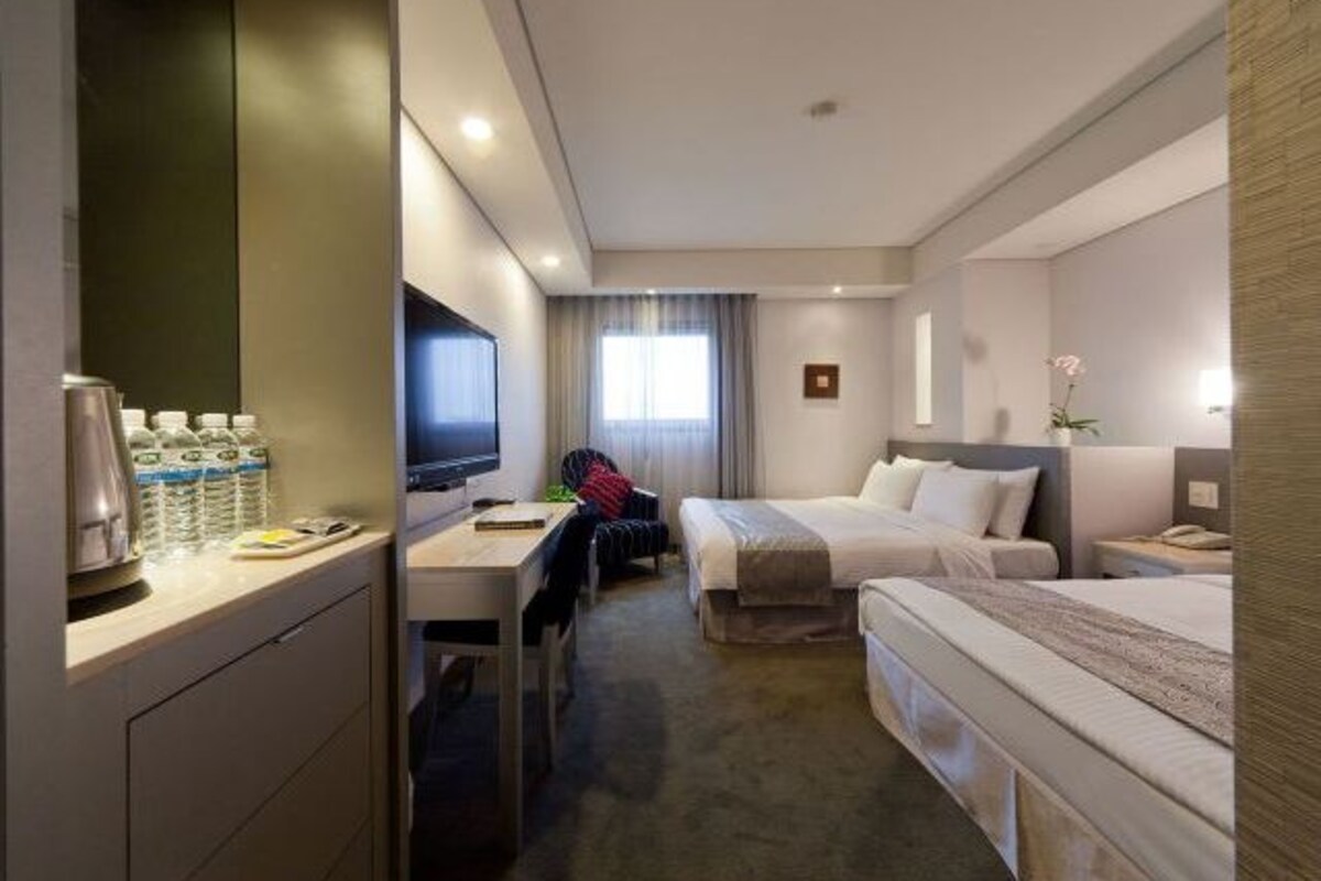 A hotel room with two beds, a desk, a chair, a TV, and a minibar.