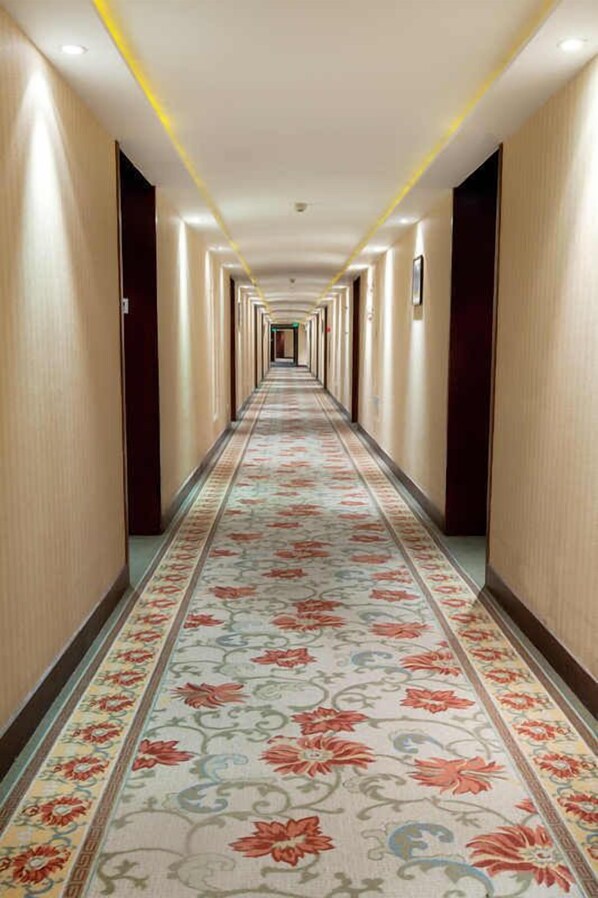 Un long couloir étroit, typique des hôtels, avec un tapis à motifs et des luminaires encastrés.