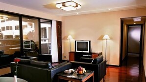 A modern hotel room with a sofa, a small table with a vase and fruit, a television, and two lamps. - Beijing HWA Apartment Hotel (Beijing)
