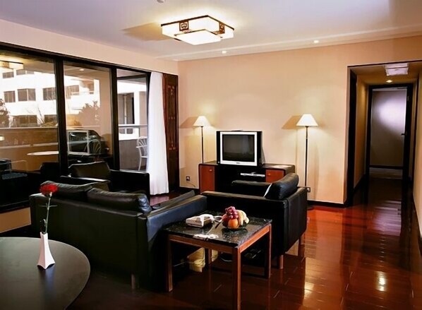 Une chambre d’hôtel moderne, équipée d’un canapé, d’une petite table avec un vase et des fruits, d’une télévision et de deux lampes.