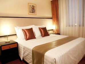 A hotel room with a large bed, two bedside tables, a nightstand, a framed picture on the wall, and a window with curtains.