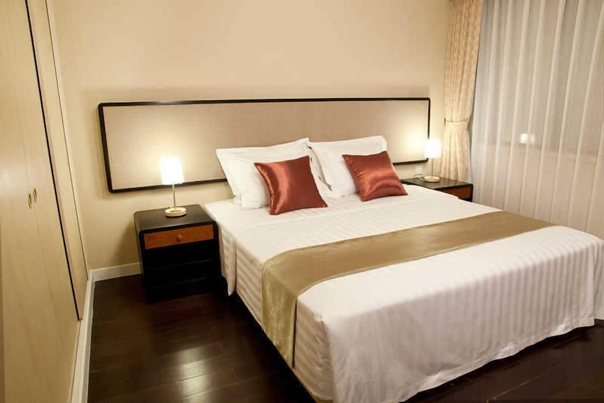 Une chambre d’hôtel avec un grand lit, deux tables de chevet et une petite table de nuit.