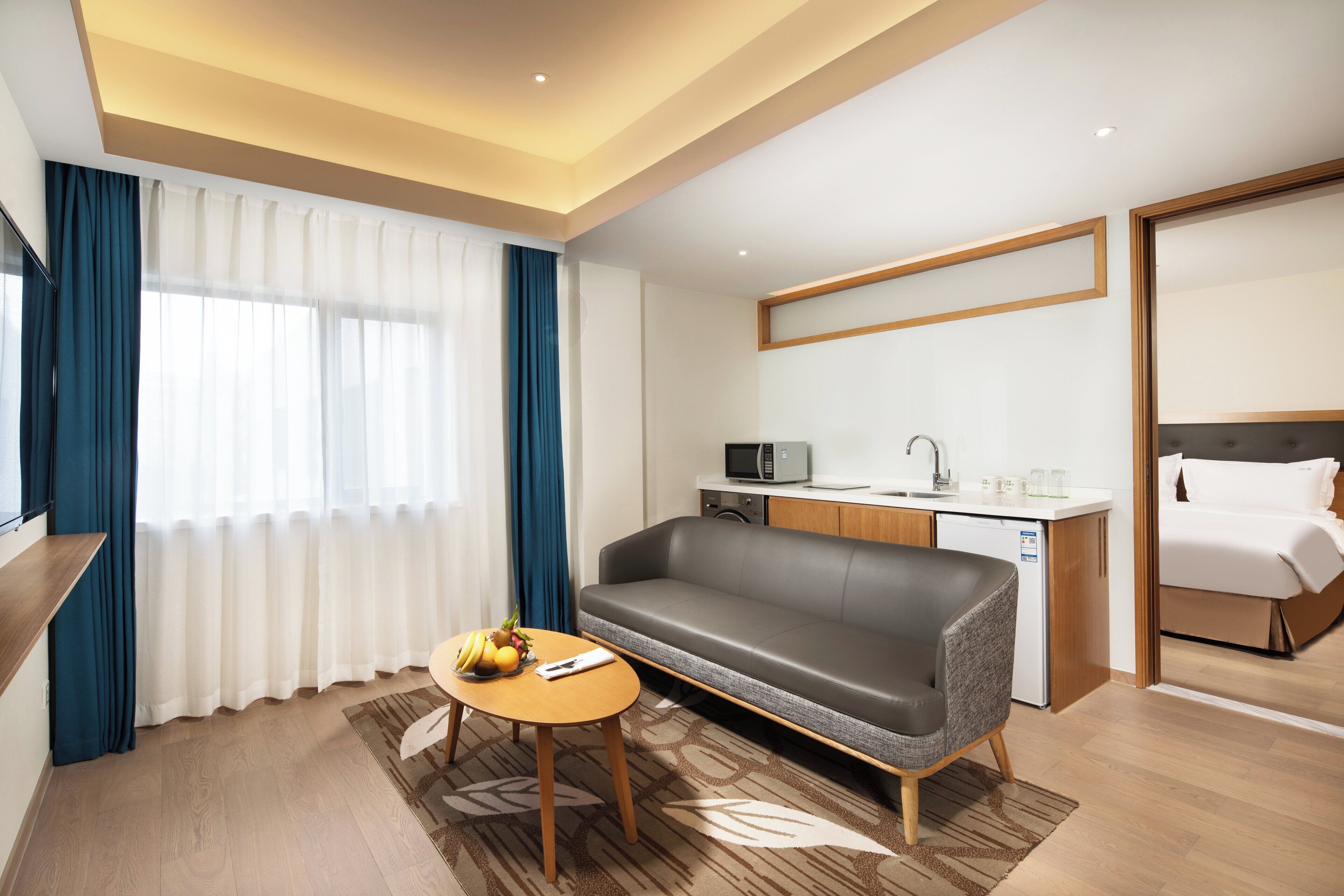 Habitación de hotel con sofá, una mesita con frutas, microondas, lavabo y cama.
