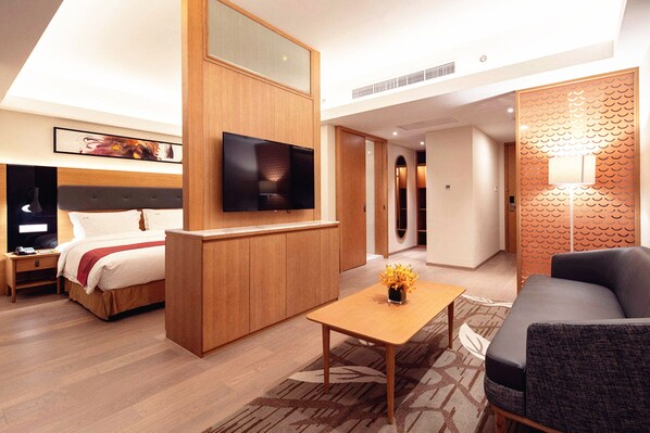 Una habitación de hotel moderna con una cama, televisor, escritorio de madera, sofá y decoración en la pared.