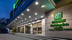 Entrada de um hotel Holiday Inn com design moderno, destacando uma placa verde e fachada bem iluminada.