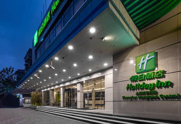 Entrada de un hotel Holiday Inn con diseño moderno, destacando un cartel verde llamativo y una fachada bien iluminada.