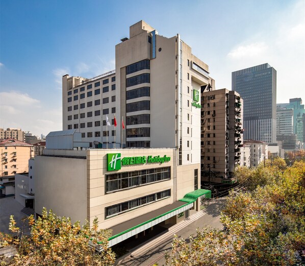 A hotel with a modern design, featuring a prominent green and white logo, multiple floors, and a flat roof.