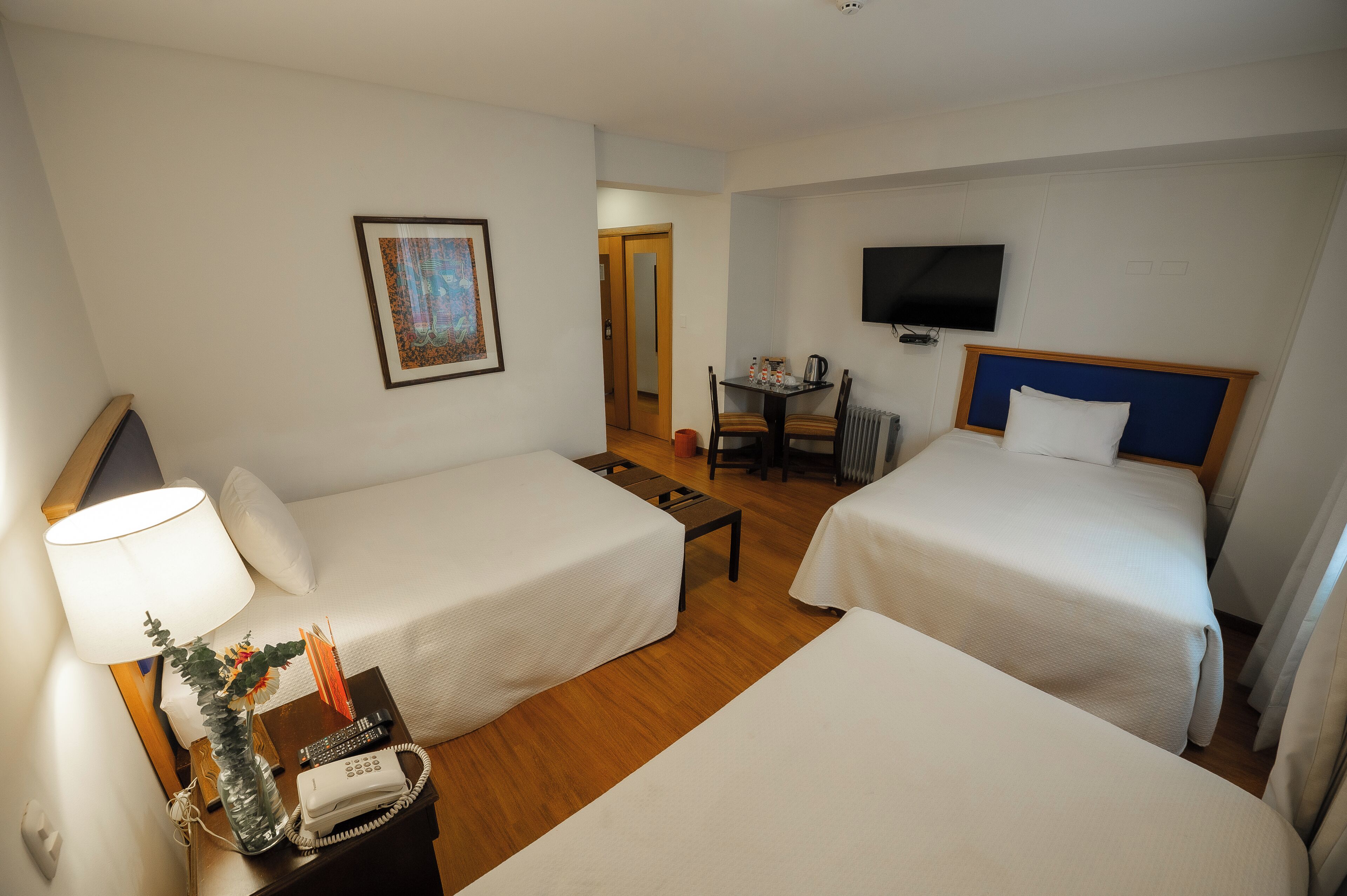 A hotel room with two beds, a desk with a chair, a television, and a painting on the wall.