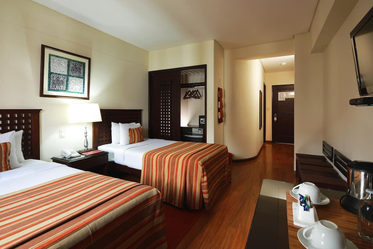 A hotel room with two beds, a desk with a lamp, a coffee maker, and a TV.