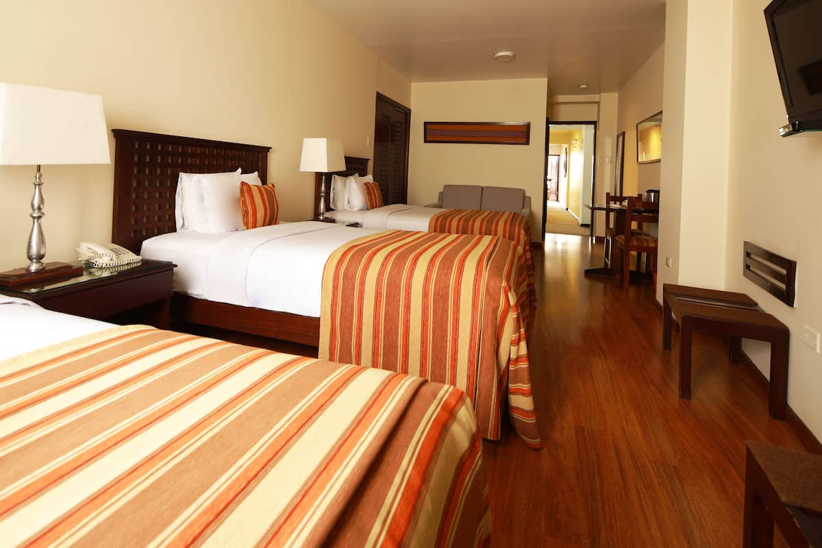 A hotel room with two beds, a desk, a chair, and a television.