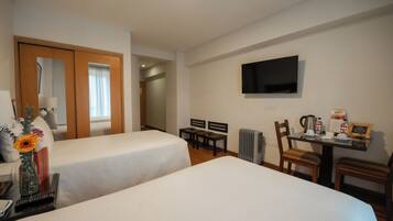 Habitación de hotel con dos camas, televisión, escritorio con hervidor y radiador.