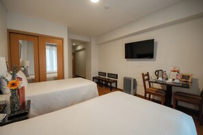 Una camera d'albergo con due letti, una televisione, una scrivania con un bollitore e un termosifone.