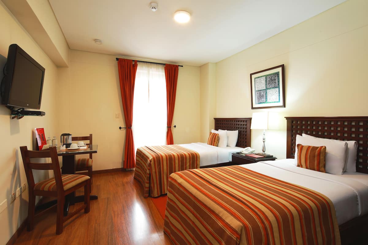 A hotel room with two beds, a desk with a chair, a television, and a window with curtains.