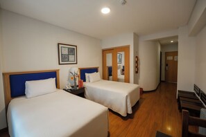Een hotelkamer met twee bedden, een nachtkastje, een lamp en een lijst met een afbeelding aan de muur.