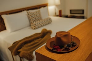 A hotel room with a neatly made bed, a brown hat, and sunglasses on a wooden nightstand. - Hotel San Agustin El Dorado (Cusco)