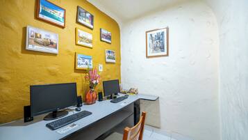 Un espacio de trabajo con dos monitores, un teclado, un florero con flores y cuadros en la pared.