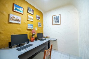 A workspace with two monitors, a keyboard, a vase with flowers, and framed pictures on the wall. - San Agustin Internacional Hotel (Cusco)