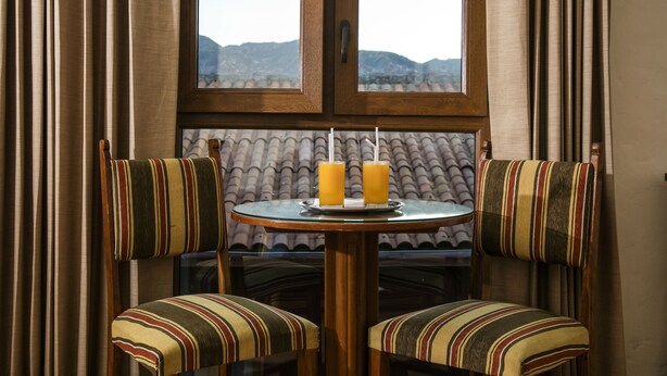 A dining area with two striped chairs, a round table, and two glasses of orange juice. - San Agustin Internacional Hotel (Cusco)