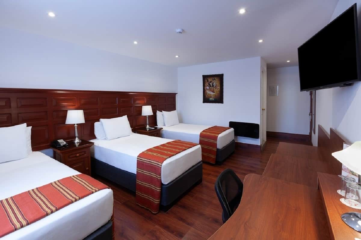 A hotel room with two beds, a desk, a chair, a flat-screen TV, and a painting on the wall.