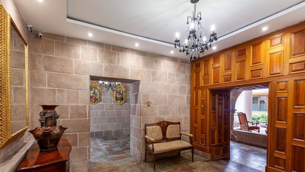 A lobby with a stone wall, a wooden bench, a table with a vase, and a chandelier. - Terra Andina Colonial Mansion (Cusco)