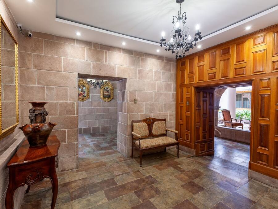 Un vestíbulo con pared de piedra, un banco de madera, una mesa con un jarrón y una araña.
