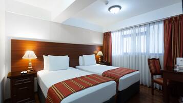 Habitación de hotel con dos camas, cabeceros de madera, un escritorio con silla y una ventana con cortinas.