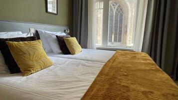 A hotel room with two beds, a large window with curtains, and a framed picture on the wall.