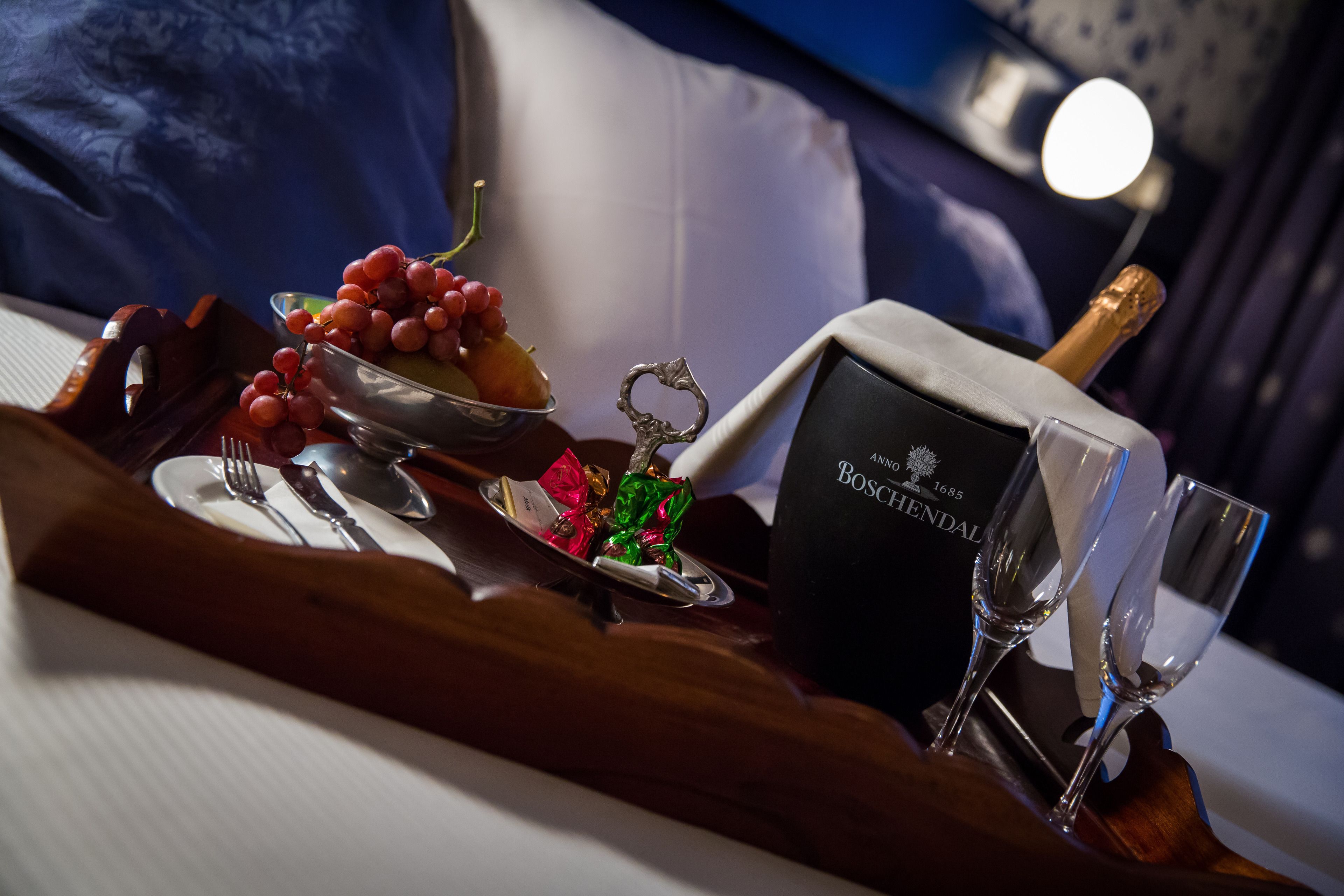 A table with a bottle of champagne, two glasses, a bowl of grapes, and a decorative item.