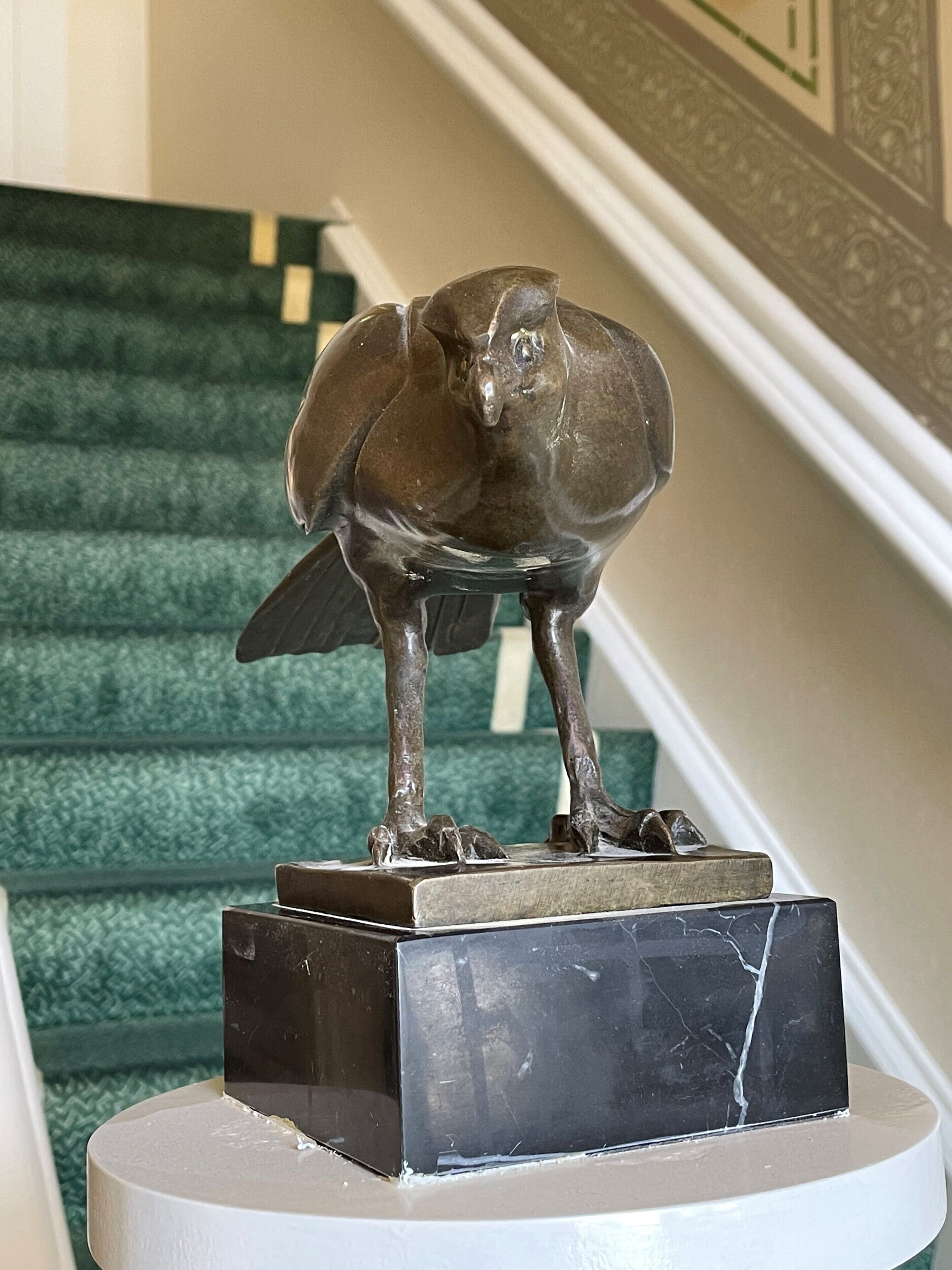 A bronze bird sculpture on a marble pedestal in a staircase area.