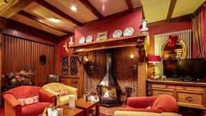 Una sala de estar acogedora con chimenea, sofás rojos y amarillos, un televisor y un espejo decorativo.