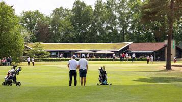 Players tee off on the lush fairway, surrounded by mature trees and a picturesque clubhouse in the distance.